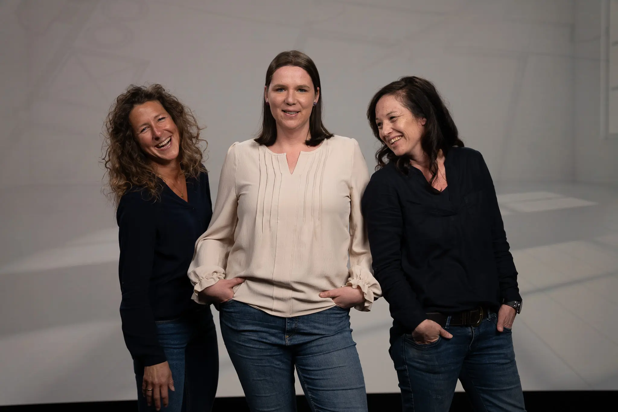 Annette Lambertz, Susanne Althoff und Sonja Hülsers stehen vor einem grauen Hintergrund und lächeln in die Kamera